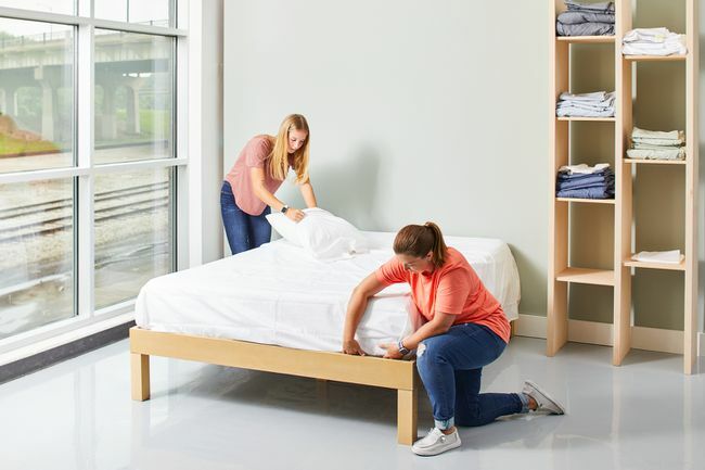 két nő ágyat készít fehér lepedővel